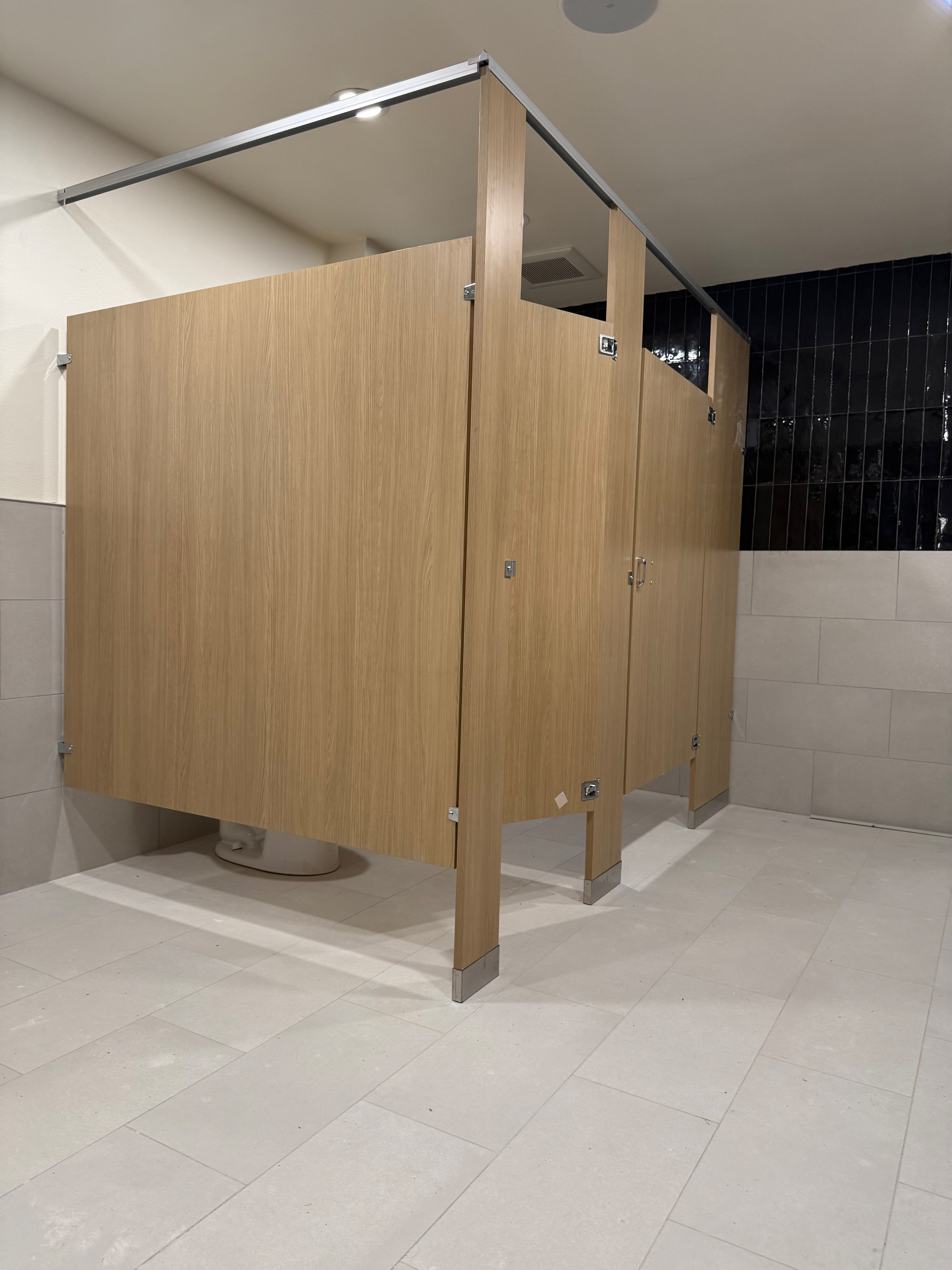 Light oak plastic laminate bathroom partitions with black tile in Plano, Texas